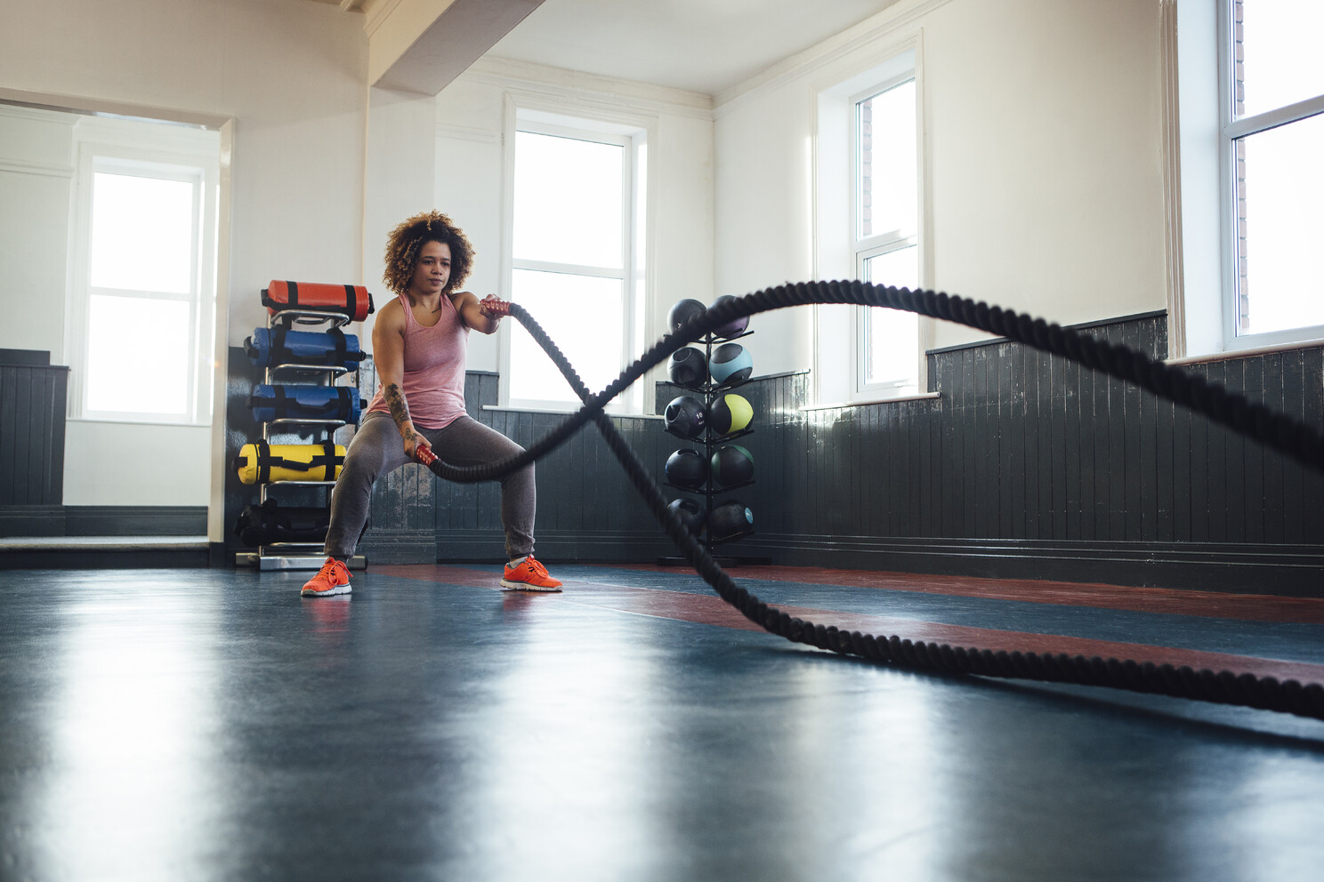 A strong woman alone in a gym, training with battle ropes